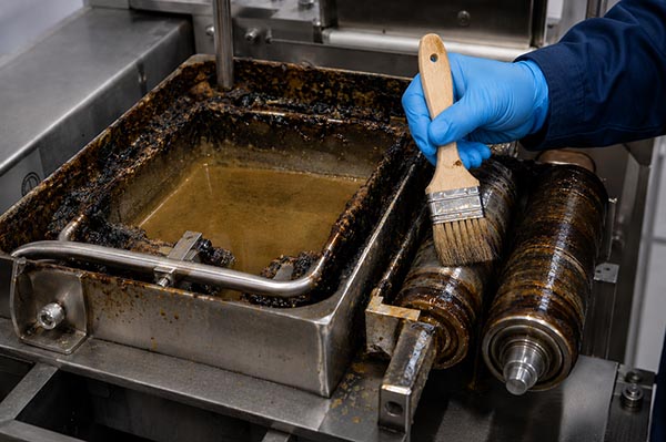 Operator cleaning glue transfer pulleys with a soft brush, showing proper technique